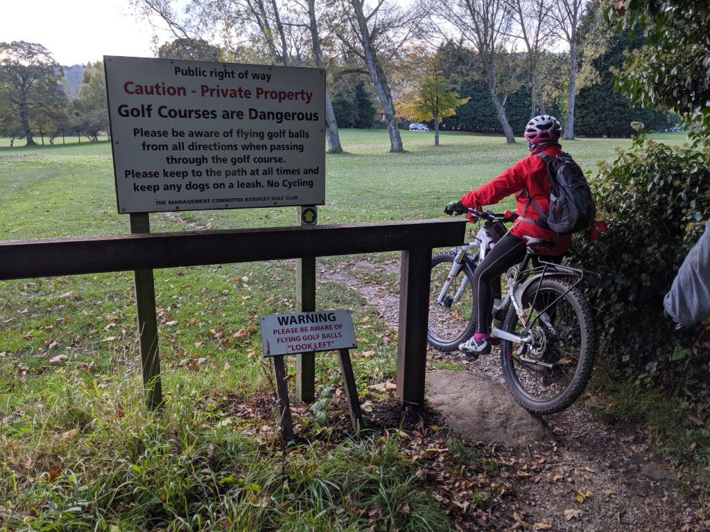 Cyclist entering golf course with sign asking to watch out for flying golf balls.