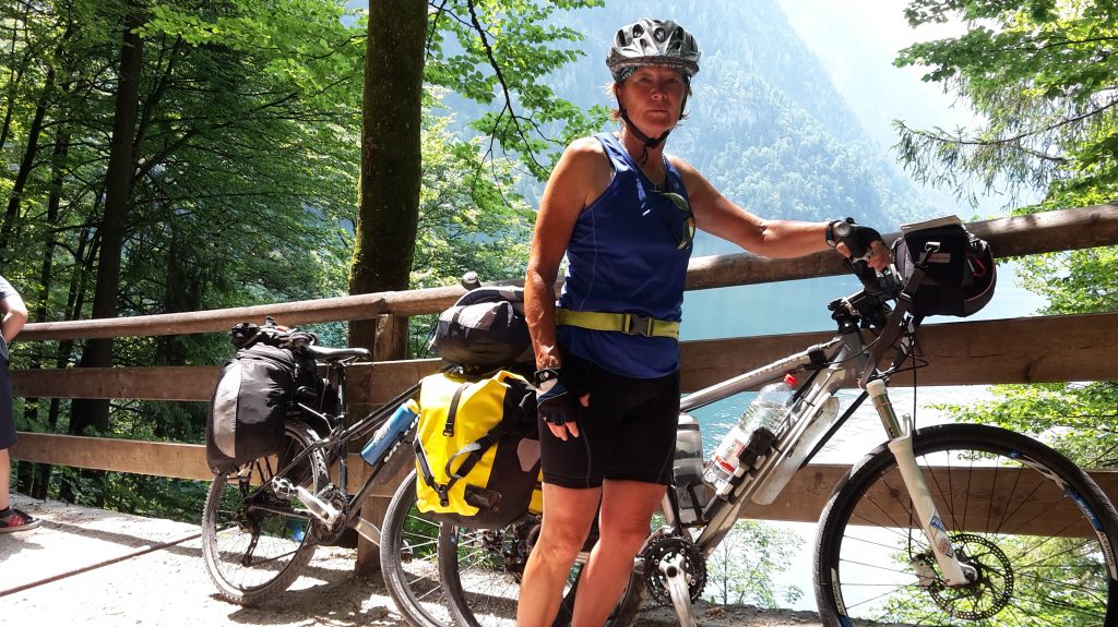 Woman standing next to a laden bike with a beautiful view in the background.