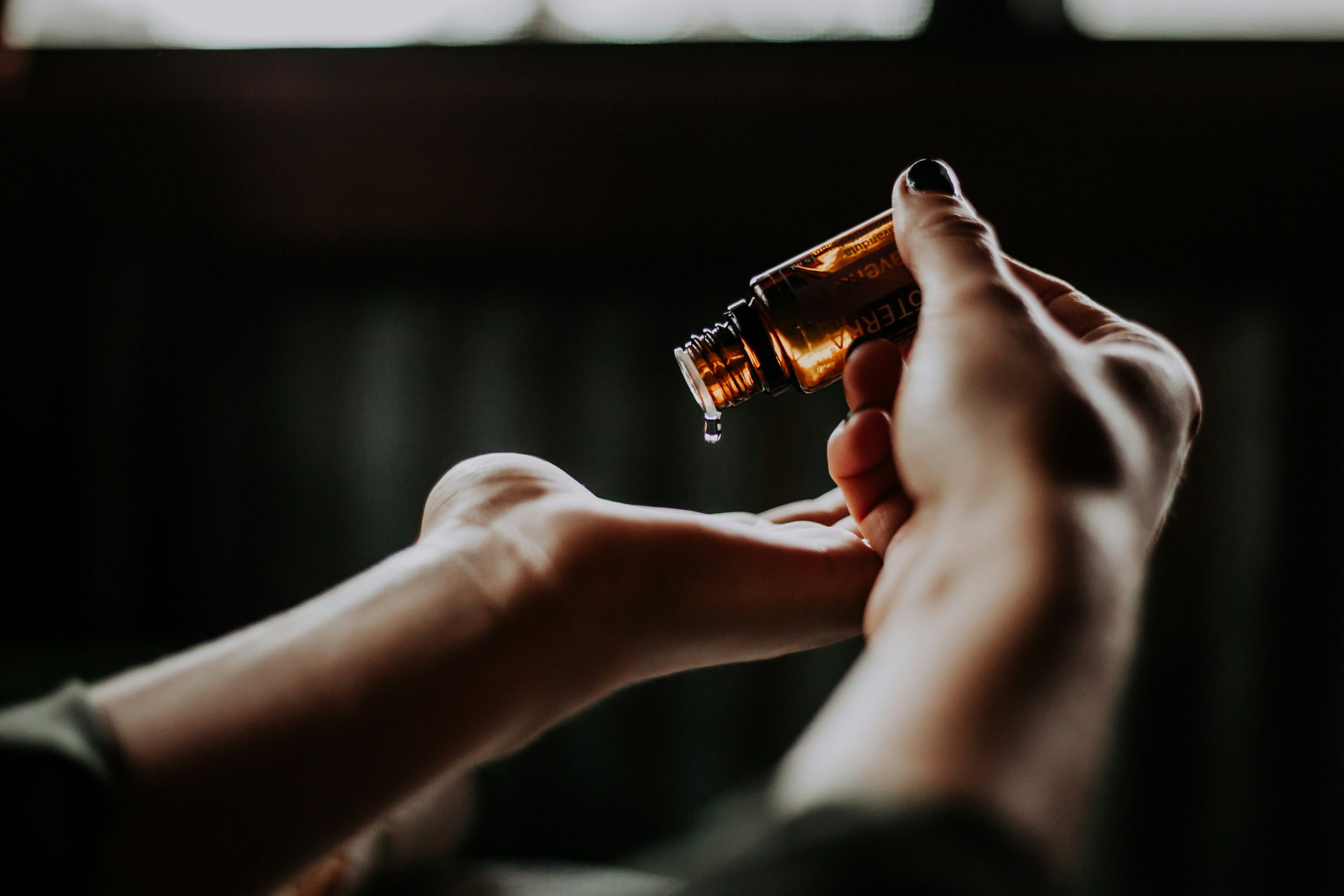 A close-up of a person’s hands as they pour drops of liquid from a small amber glass bottle onto their palm.