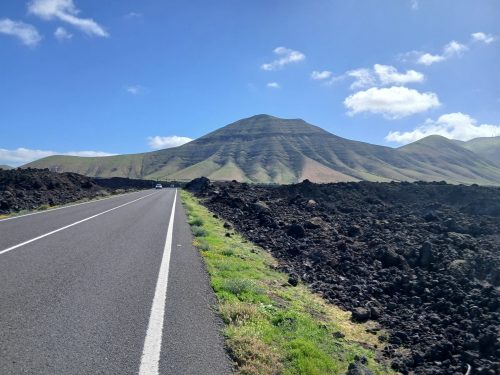 A road with a volcano and blue skies in the distance.