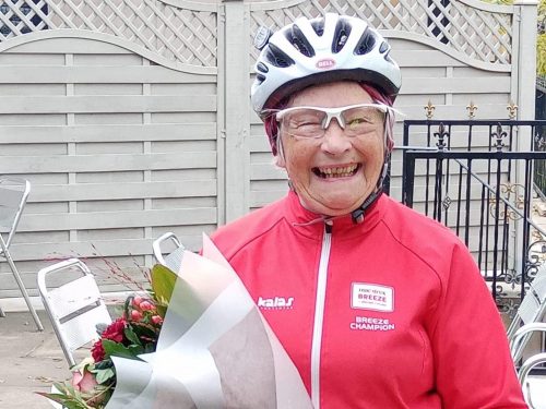 Woman in cycling gear with flowers and certificate.